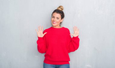 Gri grunge duvar gösterilen ve parmakları ile işaret kış kıyafeti giymiş genç yetişkin kadın kendinden emin ve mutlu gülümseyerek süre on numara.