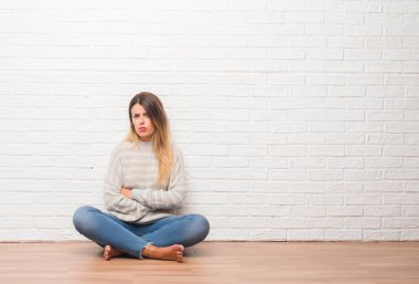 Şüpheci ve sinir, onaylamayan ifade yüz çapraz kolları üzerinde evde beyaz tuğla duvarın üzerinden katta oturan genç yetişkin kadın. Negatif kişi.