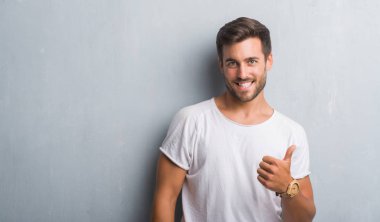 Yakışıklı delikanlı hareketi el ile mutlu yaşasın yapıyor gri grunge duvarın üzerinden. Kameraya bakarak başarı gösteren ile ifade onaylama.