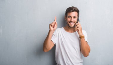 Gri grunge yakışıklı genç adam bir fikirle sürpriz telefonda konuşan duvar veya gülen yüz, bir numara ile işaret parmağı soru