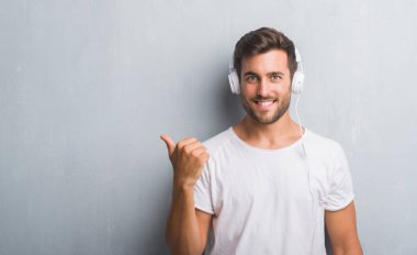 İşaret ve başparmak kadar mutlu yüz gülümseyen tarafı ile gösterilen müzik dinlerken kulaklık giyen gri grunge duvarın üzerinden yakışıklı genç