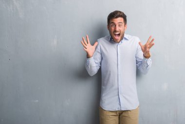 Yakışıklı genç iş adamı gri grunge üzerinde duvar deli kutluyor ve silah ile başarı için heyecanlı çığlık kaldırdı ve açık gözleri hayret giyen şık gömlek. Kazanan kavramı