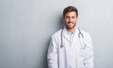 Yakışıklı genç adam yüzünde mutlu ve güzel bir gülümseme ile gri grunge duvarın üzerinden doktor. Şanslı kişi.