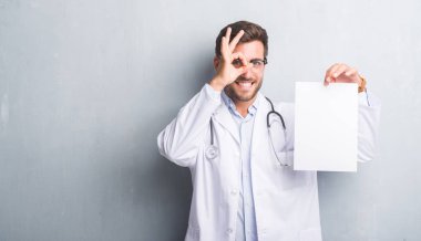 Yakışıklı genç doktor adam sayfa boş sözleşme ile ok işareti ile el parmaklarının arasından seyir göze yapıyor gülümseyen mutlu yüz tutan gri grunge duvarın üzerinden