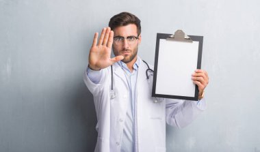 Yakışıklı genç doktor adam gri grunge duvar panosu ile tutarak açık el dur işareti ile ciddi ve kendine güvenen ifade, savunma hareketi yapıyor