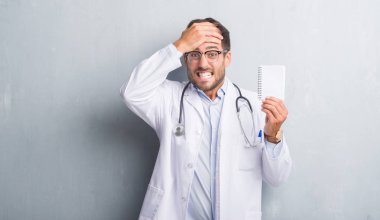 Yakışıklı genç doktor adam kafasına, el ile vurguladı boş defter tutan gri grunge duvarın üzerinden şok utanç ve sürpriz suratla, öfkeli ve sinirli. Korku ve hata için üzgün.