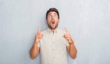 Yakışıklı delikanlı Yaz gömlek giymiş gri grunge duvarın üzerinden hayran ve yukarıya bakıyor ve parmakları ile işaret ve silah kaldırdı şaşırttı.