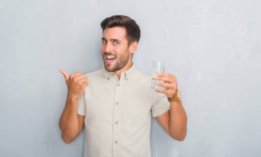 İşaret ve başparmak kadar mutlu yüz gülümseyen tarafı ile gösterilen su içme gri grunge duvarın üzerinden yakışıklı genç