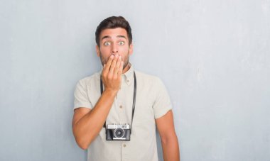 Hata, korku, sessizlik içinde gizli kavramı korkmuş ifade için utanç ile vintage fotoğraf kamera kapağı ağız eliyle tutarak gri grunge duvarın üzerinden yakışıklı genç adam şok