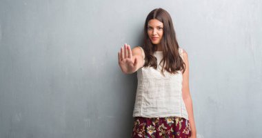 Grunge gri Duvar ile genç esmer kadın dur işareti ile ciddi ve kendine güvenen ifade, savunma hareketi yaparken el açmak