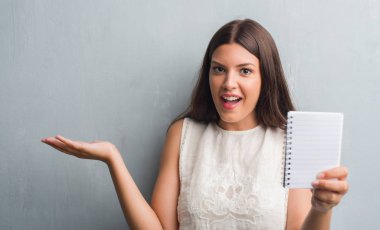 Grunge genç esmer kadın gri duvar büyük gülümseme ile çığlık ve ellerini kaldırdı kazanan ifade kutluyor zafer çok mutlu ve heyecanlı, defter gösterilen