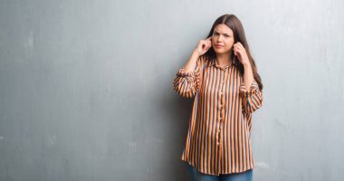 Grunge gri duvar kaplama kulakları parmakları ile yüksek sesle müzik gürültü rahatsız ifade ile genç esmer kadın. Sağır kavramı.