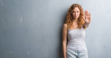 Gri grunge duvar açık eliyle dur işareti ile ciddi ve kendine güvenen ifade, savunma hareketi yaparken genç Kızıl saçlı kadın