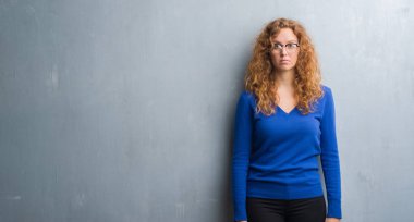 Gri grunge duvar yüzünde ciddi bir ifade ile genç Kızıl saçlı kadın. Basit ve doğal kameraya bakıyor.