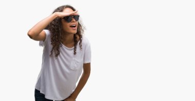 Genç İspanyol kadın çok mutlu ve gülümseyen uzakta el ile üzerine kafa seyir güneş gözlüğü takıyor. Arama kavramı.