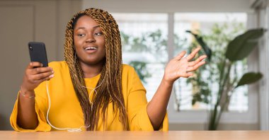 Afrikalı-Amerikalı kadın Smartphone ile büyük gülümseme ile çığlık zaferini kutluyor ve ellerini kaldırdı kulaklıklar çok mutlu ve heyecanlı, kazanan ifade kullanma