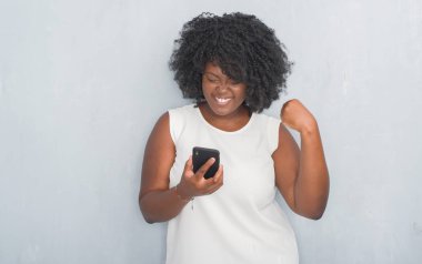 Gri grunge genç Afro-Amerikan kadın duygu tezahürat gurur çığlık ve zafer ve başarı çok heyecanlı, kutluyor smartphone kullanarak bir mesaj manifatura duvar