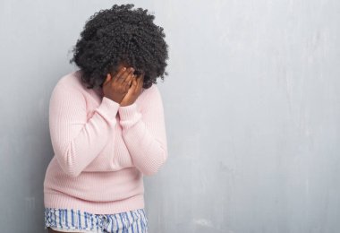 Genç Afro-Amerikan artı boyutu kadın ağlayarak süre elleriyle yüzünü kapsayan üzgün ifade ile kış kazak giyen gri grunge duvarın üzerinden. Depresyon kavramı.