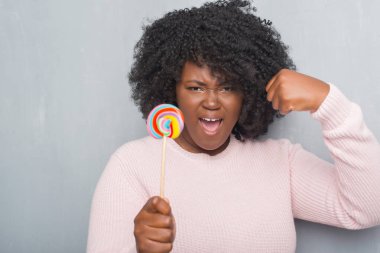 Lolipop yemek gri grunge duvarın üzerinden genç Afro-Amerikan kadın şeker ile öfke, çılgın ve yükseltilmiş eliyle diye bağıran rahatsız ve hayal kırıklığına uğramış öfke kavramı bağırarak