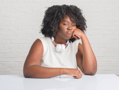 Düşünme seyir yorgun ve sıkılmış depresyon sorunları ile kulaklıklar giyen masada oturan genç Afro-Amerikan kadın kolları geçti.