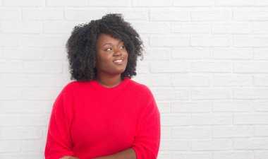 Genç Afro-Amerikan artı boyutu kadın görünümlü yan ve dik dik bakma uzağa düşünce gülümseyen beyaz tuğla duvarın üzerinden.
