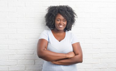 Genç Afro-Amerikan artı beyaz tuğla boyutu kadın mutlu yüz çapraz silah kameraya bakarak ile gülümseyen duvar. Olumlu bir kişi.