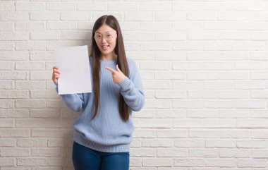 Boş kağıt çok mutlu el ve parmak ile işaret tutan tuğla duvarın üzerinden Genç Çinli kadın