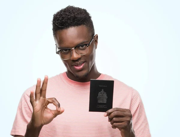 優秀なシンボルの指で サインをしているカナダのパスポートを保持して若いアフリカ系アメリカ人 — ストック写真