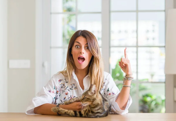 Young woman at home playing with her cat surprised with an idea or question pointing finger with happy face, number one