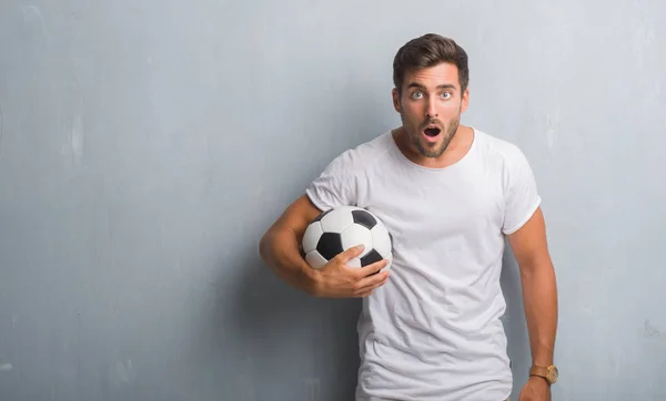 驚き顔 恐怖表現と興奮とショックで怖いサッカー サッカー ボールを保持している灰色のグランジの壁を越えてハンサムな若い男 — ストック写真