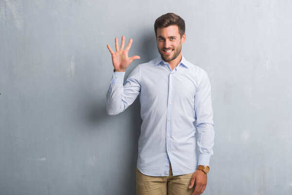 Красивый молодой бизнесмен на серой гранж-стене, одетый в элегантную рубашку и показывающий пальцами номер пять, улыбаясь уверенно и счастливо
.