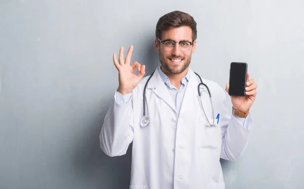 Pohledný Mladý Lékař Muž Přes Zeď Šedá Grunge Držení Smartphone — Stock fotografie