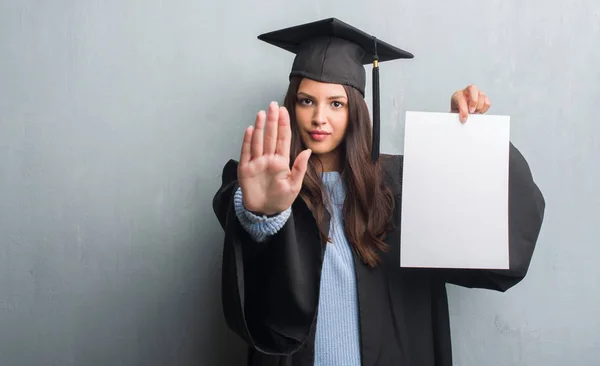 Jovem Morena Sobre Grunge Parede Cinza Vestindo Graduado Uniforme Segurando — Fotografia de Stock