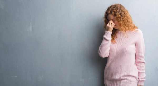 若い赤毛ピンク グレー グランジ壁を着て向こうの女性のセーターが疲れて鼻 疲労や頭痛を感じて目をこするします ストレスと欲求不満のコンセプト — ストック写真