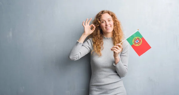 優秀なシンボルの指で サインをしているポルトガルの旗を保持している灰色のグランジの壁を越えて若い赤毛の女性 — ストック写真