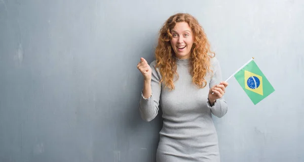 灰色垃圾墙上的年轻红头发的女人拿着巴西国旗尖叫着自豪和庆祝胜利和成功非常兴奋 欢呼的情绪 — 图库照片