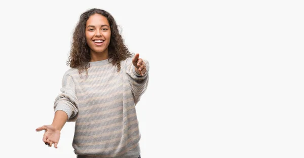 美しい若いヒスパニック系女性の抱擁の両手を広げて笑みを浮かべてカメラを見てのストライプのセーターを着ています 晴れやかな表情の受け入れ幸せ — ストック写真