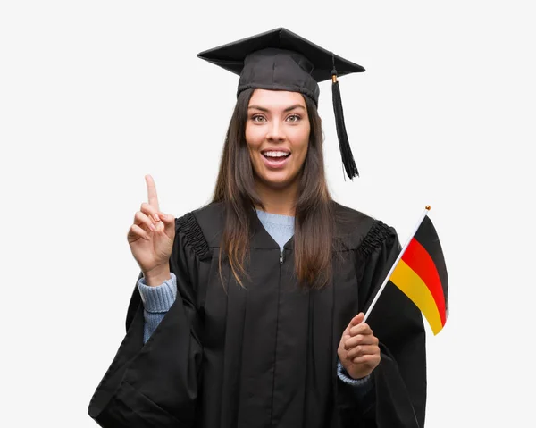 Mujer Hispana Joven Vistiendo Uniforme Graduado Sosteniendo Bandera Alemania Sorprendida — Foto de Stock