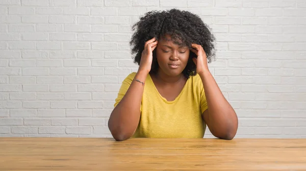 Young african american woman sitting on the table at home with hand on head for pain in head because stress. Suffering migraine.