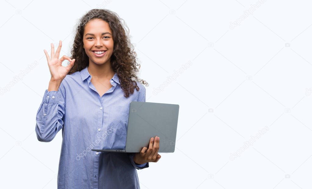 Young hispanic woman holding computer laptop doing ok sign with fingers, excellent symbol
