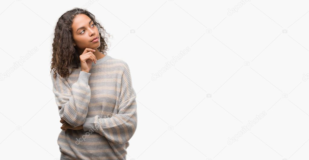 Beautiful young hispanic woman wearing stripes sweater with hand on chin thinking about question, pensive expression. Smiling with thoughtful face. Doubt concept.