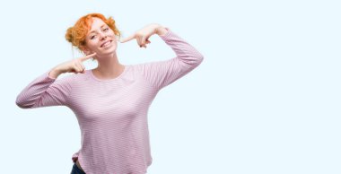 Kendinden emin gösterilen ve işaret parmakları diş ve ağız ile gülümseyen genç Kızıl saçlı kadın. Sağlık kavramı.