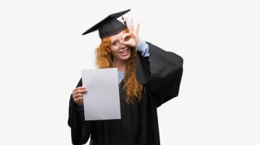 Derecesi ile ok işareti ile el parmaklarının arasından seyir göze yapıyor gülümseyen mutlu yüz tutan lisansüstü üniforma giyen genç Kızıl saçlı kadın