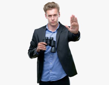 Genç yakışıklı sarışın adam dürbünle bakarak dur işareti ile ciddi ve kendine güvenen ifade, savunma hareketi yaparken el açmak