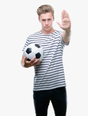 Genç yakışıklı sarışın adam açık eliyle dur işareti ile ciddi ve kendine güvenen ifade, savunma jest yapıyor futbol topu tutan