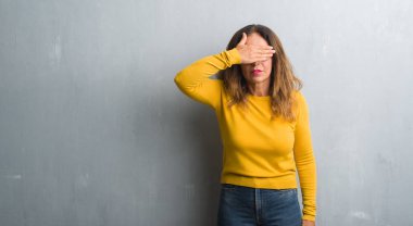 Orta yaş İspanyol kadın gülümsüyor ve gözleri için sürpriz kapsayan yüz el ile gülüyor gözlüklü gri duvar yüzünden. Kör kavramı.