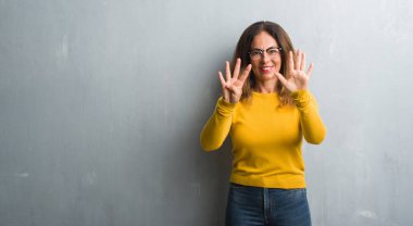 Gri duvar gösterilen ve parmakları ile işaret gözlük takan orta yaş İspanyol kadın numara 9 kendinden emin ve mutlu gülümseyerek süre.