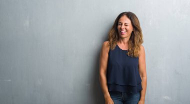Orta yaş İspanyol kadın seksi bir ifadeyle, neşeli ve mutlu yüzünü kameraya bakarak göz kırpıyor gri grunge duvarın üzerinden ayakta.