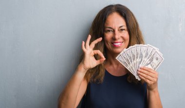 Orta yaş İspanyol kadın parmakları, mükemmel sembolü olan ok işareti yapıyor dolar tutan gri grunge duvarın üzerinden ayakta