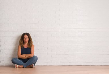 Orta yaş İspanyol kadın beyaz tuğla duvar şüpheci ve sinir, onaylamayan ifade yüz çapraz kolları üzerinde yere oturma. Negatif kişi.